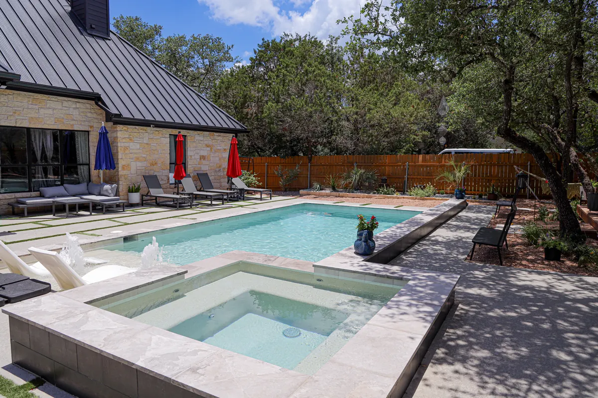Pool and spa framed by a stone home and trees