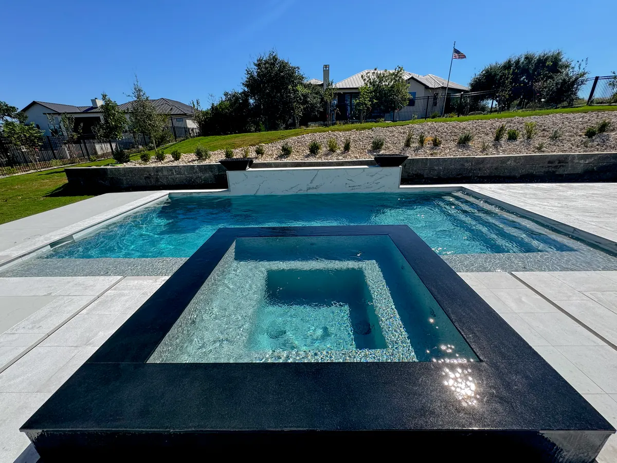 Dark raised spa overlooking a rectangular pool and white feature wall